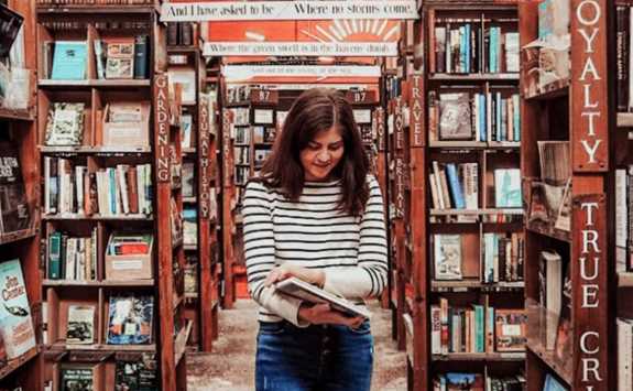 Melis Besen, PhD student at Newcastle University Business School, standing in a library surrounded by bookshelves.